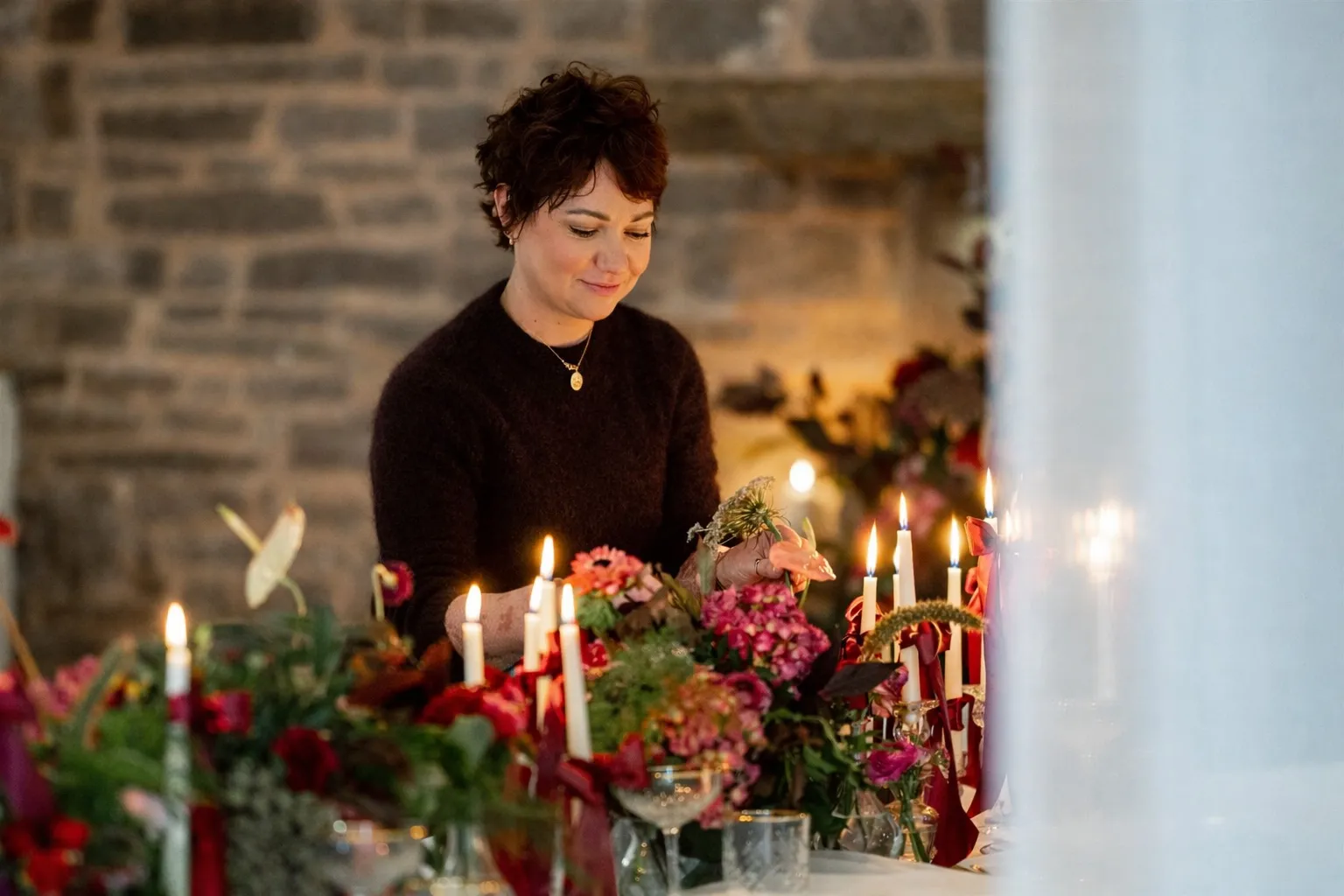 Catrin arranging deep red flowers by candlelight