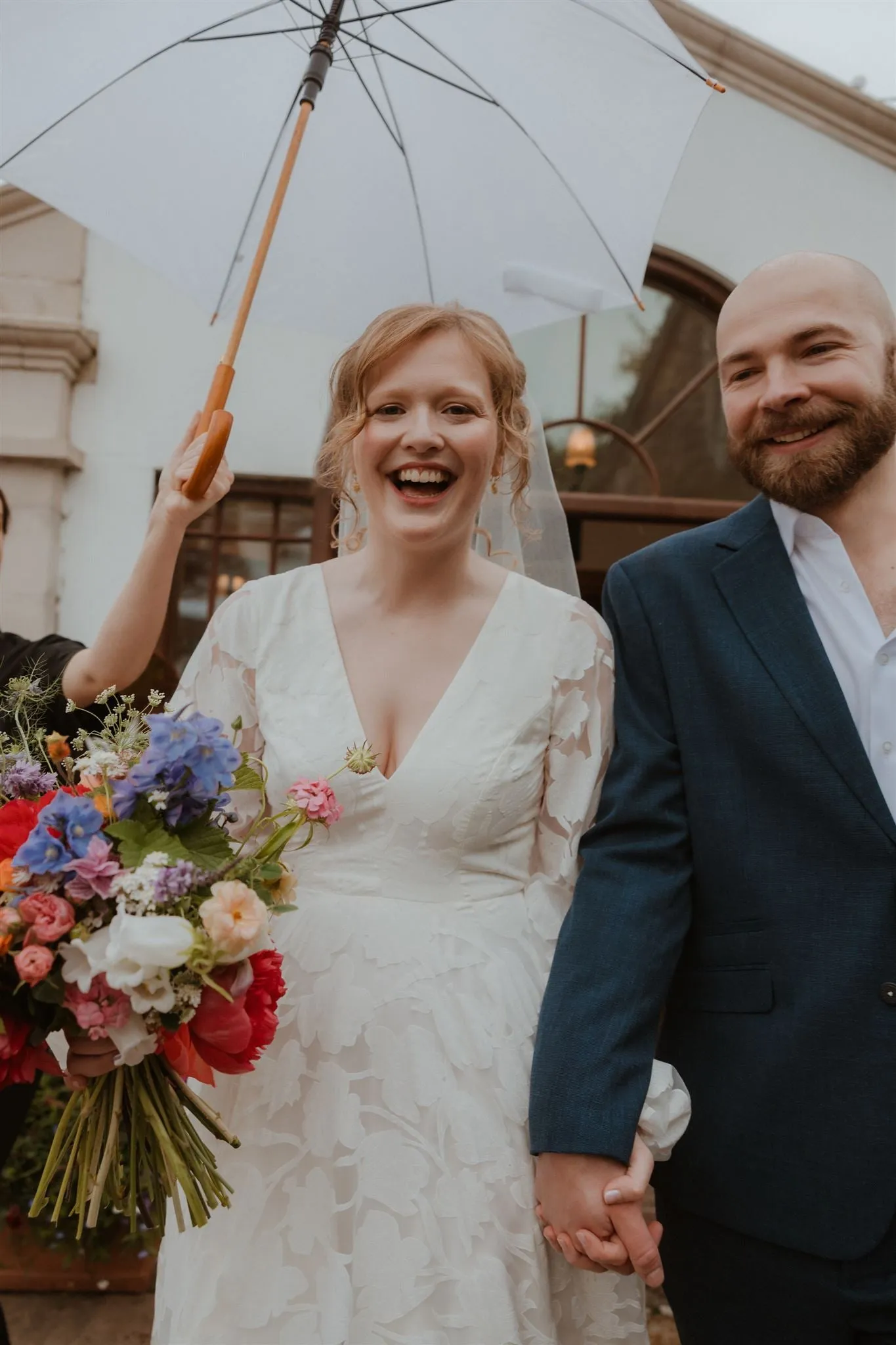 A couple under a clear umbrella with a pastel bouquet